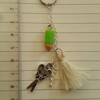 Porte-clef avec: ciseaux, crayon vert et pompon crème en coton. Longueur totale environ 8 cm.