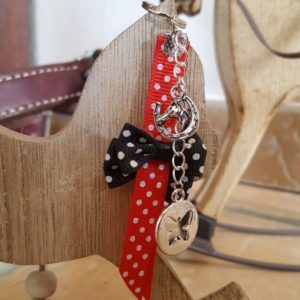 Bijoux de sac avec fermeture anneau 1,5 cm. Galon rouge à poids blancs et petits nœuds noirs à poids blancs. Charm breloque papillon. Longueur totale environ 10 cm